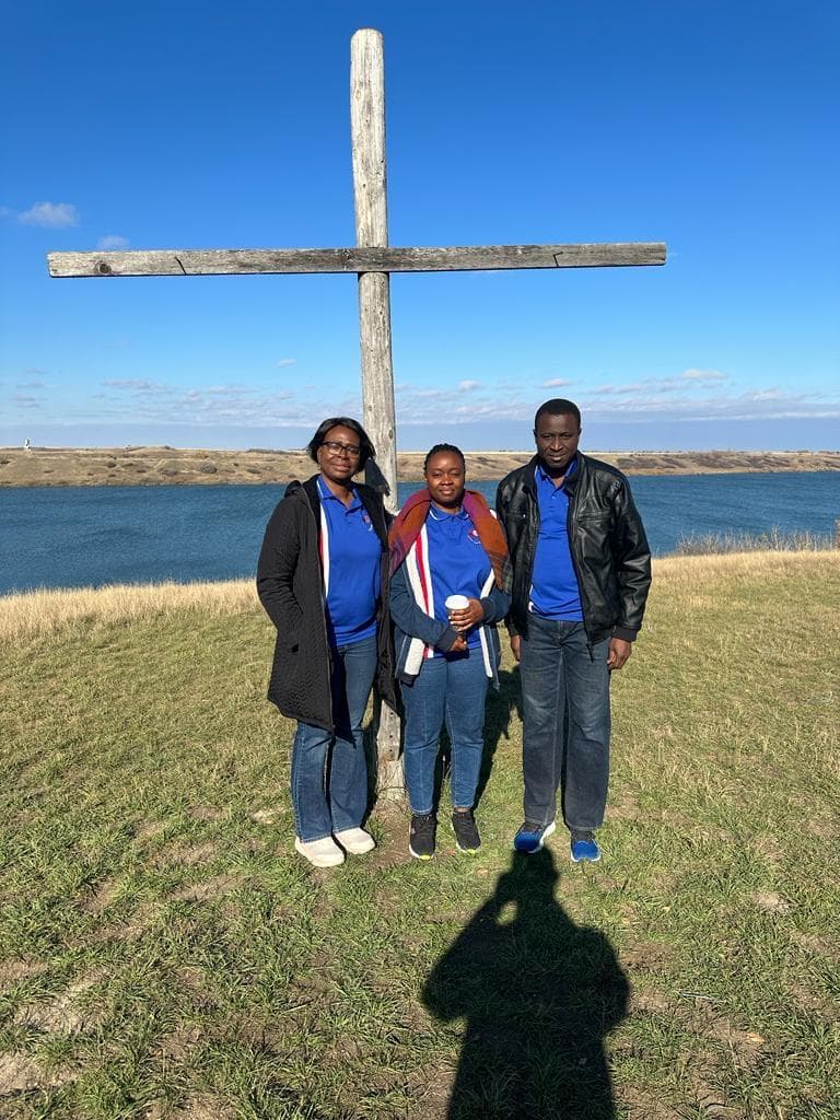 Three retreat participants standing beside a wooden cross overlooking the water
