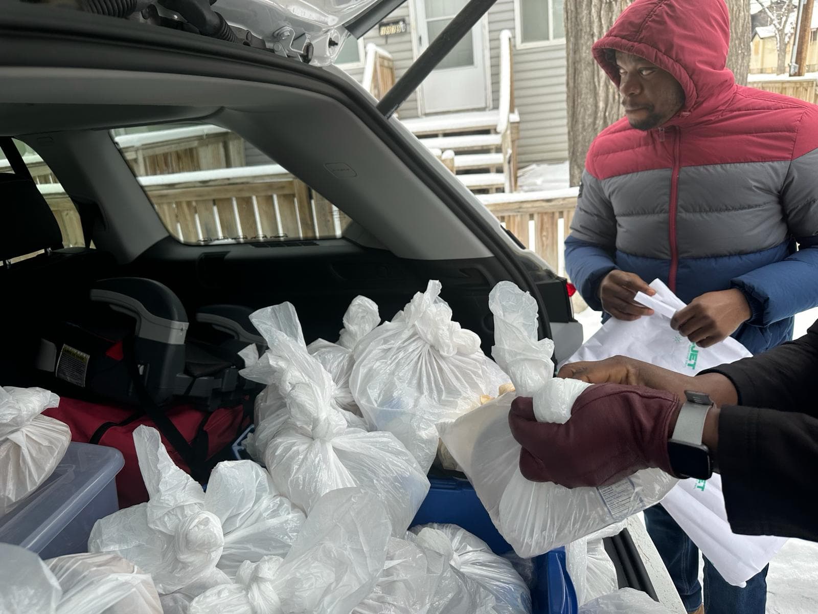 A volunteer preparing bags of food beside an open vehicle during winter outreach